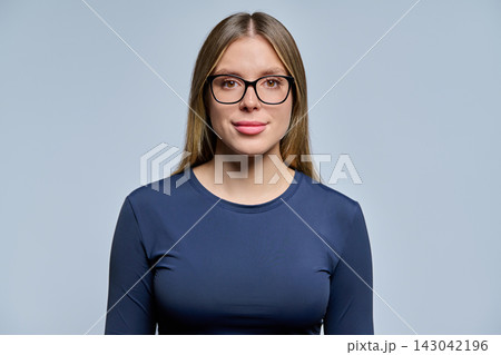 Young woman in eyeglasses looking at camera on studio gray background Young woman in eyeglasses looking at camera on studio gray background 143042196
