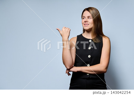 Businesswoman pointing thumb to copy space standing on gray background Businesswoman pointing thumb to copy space standing on gray background 143042254