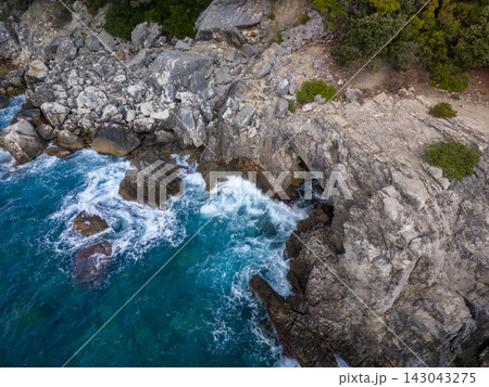 Rocky coast at Aquarium Bay in Albania with waves crashing below rugged cliffs. Turquoise water foams against stone ledges, creating dramatic natural seascape with wild, remote mood. 143043275