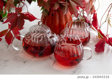 Autumn tea ritual cozy warm beverage in glass teapot and cups with red leaves decoration Autumn tea ritual cozy warm beverage in glass teapot and cups with red leaves decoration 143043318