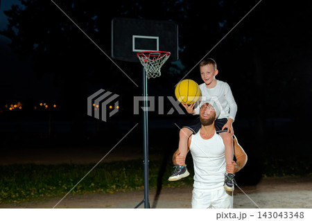 A father and son share a fun moment playing basketball outdoors at night with a hoop in the background A father and son share a fun moment playing basketball outdoors at night with a hoop in the background 143043348