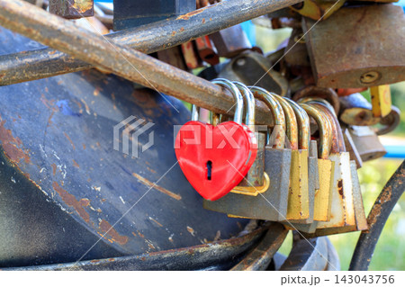 Heart-shaped metal red love locks attached to bridge railings. Iron padlocks that newlyweds hang outdoors. Heart-shaped metal red love locks attached to bridge railings. Iron padlocks that newlyweds hang outdoors. 143043756