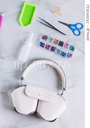 The process of decorating a headphone case with colorful rhinestones on a table top and vertical view 143043812