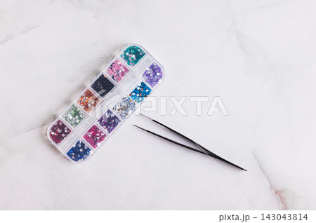 A box of assorted colorful decorative rhinestones and tweezers on the table top view A box of assorted colorful decorative rhinestones and tweezers on the table top view 143043814