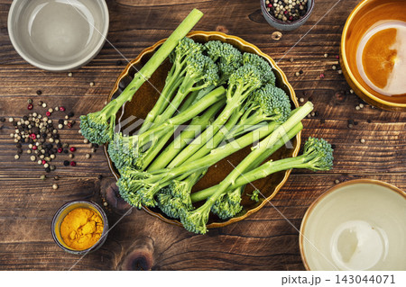 Organic Baby Broccoli Stalks with Seasonings on Kitchen Table. 143044071