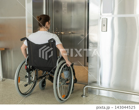 A Caucasian woman in a wheelchair uses an elevator. A Caucasian woman in a wheelchair uses an elevator. 143044525
