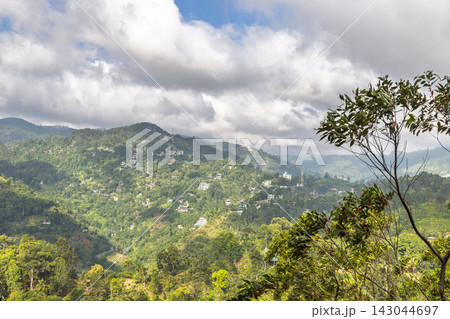 Verdant Mountain Landscape with Scattered Houses Under a Broad, Cloudy Sky on a Bright Day. Mountain landscape near Ella in Sri Lanka. Verdant Mountain Landscape with Scattered Houses Under a Broad, Cloudy Sky on a Bright Day. Mountain landscape near Ella in Sri Lanka. 143044697