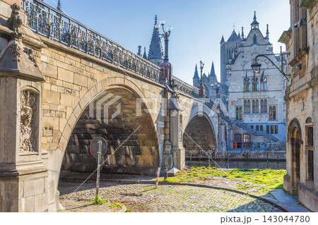 Historic St. Michael's Bridge in Ghent town in Belgium, Europe. Historic Stone Bridge Archway Over Water with Ornate Building and Cobblestone Street in European City Historic St. Michael's Bridge in Ghent town in Belgium, Europe. Historic Stone Bridge Archway Over Water with Ornate Building and Cobblestone Street in European City 143044780