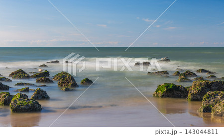 Tranquil Coastal Scene with Moss-Covered Rocks and Serene Sea Water Under a Clear Blue Sky at Sunset or Sunrise Time. Ostend, a coastal city in Belgium, Europe. 143044811
