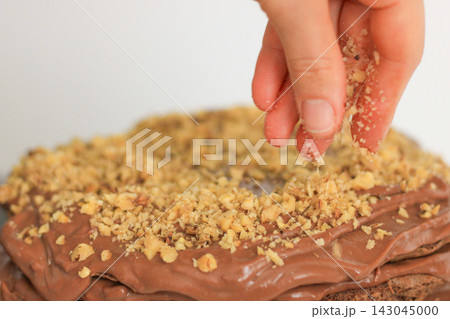 A hand spreading nuts on homemade chocolate cake A hand spreading nuts on homemade chocolate cake 143045000