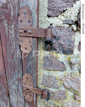 An old, rusty metal hinge on the wooden door of a stone building. An old, rusty metal hinge on the wooden door of a stone building. 143045280
