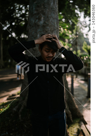Young man holding head in hands outdoors Young man holding head in hands outdoors 143046360