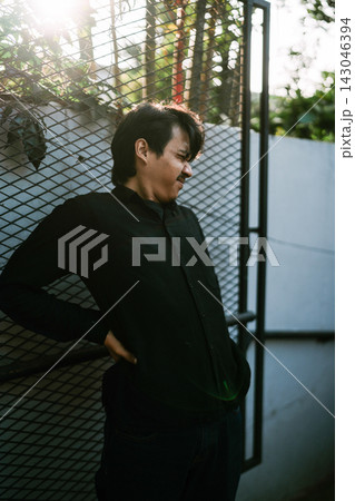 Man leaning against metal fence in sunlight Man leaning against metal fence in sunlight 143046394