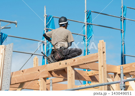 新築木造住宅の上棟。梁の上で建方作業をする大工職人の後ろ姿 新築木造住宅の上棟。梁の上で建方作業をする大工職人の後ろ姿 143049051