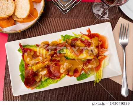 Pork bacon ham slices are baked with young, crisp cogollos lechuga hearts and seasoned with mustard sauce. 143049859