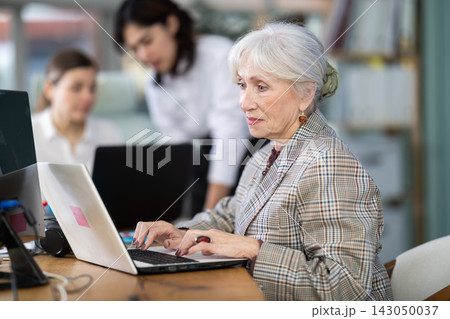 Elderly woman works on laptop with female colleagues Elderly woman works on laptop with female colleagues 143050037