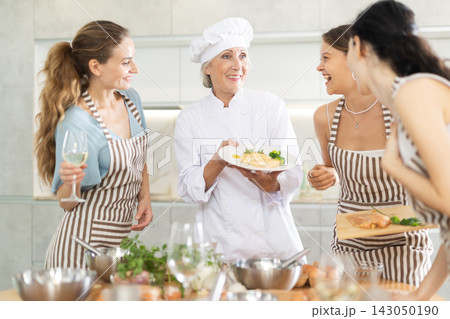 Mature female cook holding plate with cooked chicken Mature female cook holding plate with cooked chicken 143050190