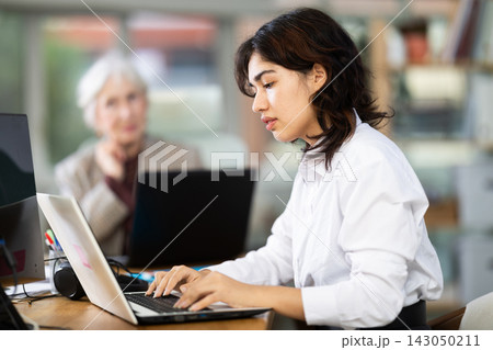 In office, young Asian woman is working on laptop as part of group of colleagues. In office, young Asian woman is working on laptop as part of group of colleagues. 143050211