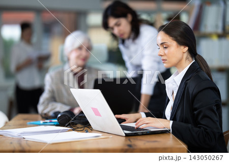 In office, young woman is working on laptop as part of group of colleagues. In office, young woman is working on laptop as part of group of colleagues. 143050267