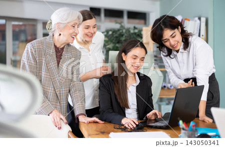 Group of women colleagues look at laptop screen and laugh Group of women colleagues look at laptop screen and laugh 143050341