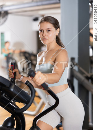 Sporty girl working out on elliptical machine in gym. Healthy active lifestyle concept Sporty girl working out on elliptical machine in gym. Healthy active lifestyle concept 143050450