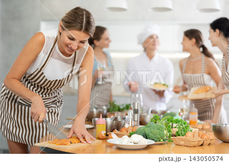 Young woman cutting raw chicken breast 143050574