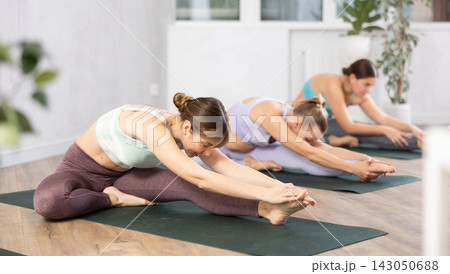 Active women perform a stretching exercise in a pose Janu Shirshasana Active women perform a stretching exercise in a pose Janu Shirshasana 143050688