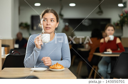 Young girl enjoying coffee and croissant in cafeteria Young girl enjoying coffee and croissant in cafeteria 143050701
