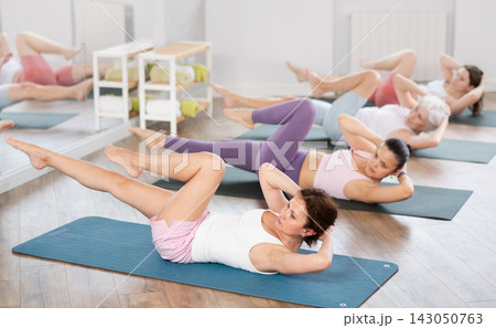 Athletic women doing pilates or aerobics - doing back exercises during group training in gym Athletic women doing pilates or aerobics - doing back exercises during group training in gym 143050763