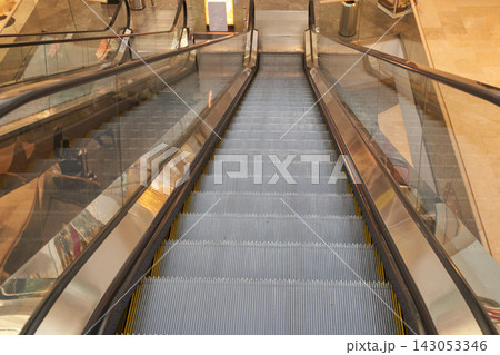 Empty Escalator Descending To Lower Level In Shopping Mall With Metal Steps Glass Side Panels Warm Empty Escalator Descending To Lower Level In Shopping Mall With Metal Steps Glass Side Panels Warm 143053346