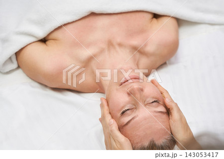 Woman Receiving Facial Massage With Eyes Closed Under White Blanket In Calm Spa Treatment Room 143053417