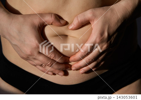 Person Shaping Heart With Hands Around Lower Abdomen In Dark Studio Close-Up With Black Waistband 143053601
