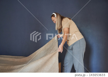 Woman Wearing White Headphones Leaning Forward Arranging Blanket Over Bed Frame In Compact Bedroom Woman Wearing White Headphones Leaning Forward Arranging Blanket Over Bed Frame In Compact Bedroom 143053633