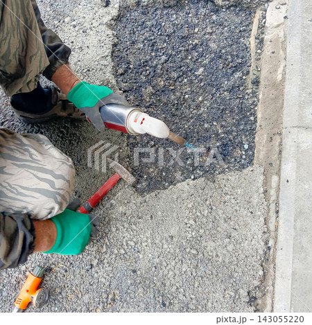 Worker repairing asphalt pavement with a gas torch and hand tools 143055220