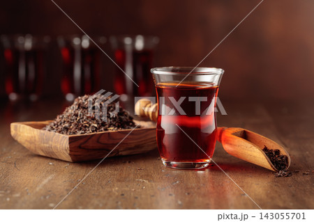 Glass transparent cup of black tea and dry tea in old wooden dish. 143055701