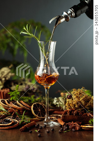 Herbal bitter liqueur is poured from a dark glass vintage bottle into a glass. Herbal bitter liqueur is poured from a dark glass vintage bottle into a glass. 143055705