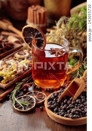 Rustic herbal tea with anise, dried citrus, juniper berries and aromatic spices in a glass mug. 143055710