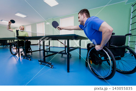 Adult disabled men in a wheelchair playing table tennis Adult disabled men in a wheelchair playing table tennis 143055835