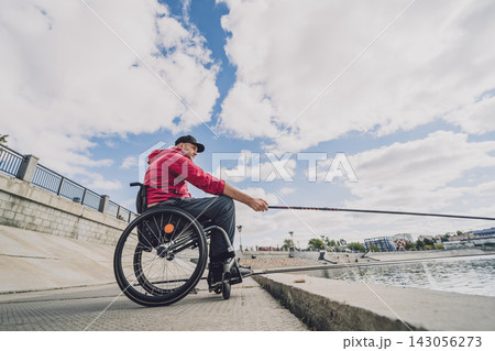 Person with a physical disability in a wheelchair fishing from fishing pier. 143056273