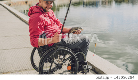 Person with a physical disability in a wheelchair fishing from fishing pier. 143056284