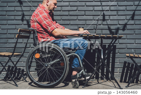 Freelancer with a physical disability in a wheelchair working at the street cafe Freelancer with a physical disability in a wheelchair working at the street cafe 143056460