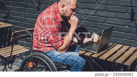 Freelancer with a physical disability in a wheelchair working at the street cafe Freelancer with a physical disability in a wheelchair working at the street cafe 143056461