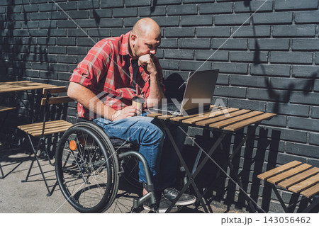 Freelancer with a physical disability in a wheelchair working at the street cafe 143056462