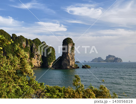 Limestone sea stack rising from turquoise coastal waters framed by dense green foliage Limestone sea stack rising from turquoise coastal waters framed by dense green foliage 143056819