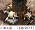 Rusty metal pipe support with three roller wheels on weathered wooden deck in sunlight 143056838