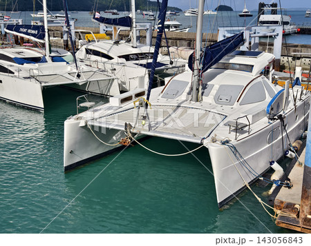 Wide marina crowded with moored sailboats and catamarans beneath partly cloudy blue sky Wide marina crowded with moored sailboats and catamarans beneath partly cloudy blue sky 143056843