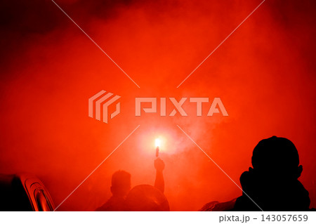 Silhouetted figure holding a lit red flare in thick smoke at night 143057659