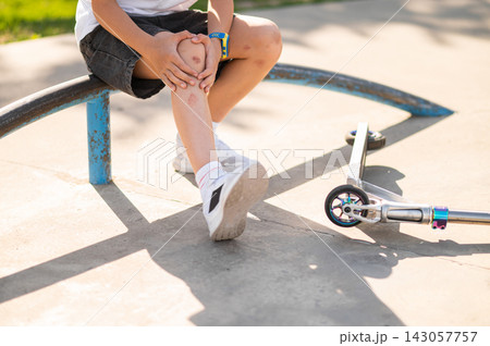 Boy in a hat sitting on the ground near the scooter after a fall down Boy in a hat sitting on the ground near the scooter after a fall down 143057757