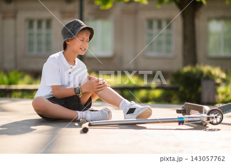Boy in a hat sitting on the ground near the scooter after a fall down 143057762