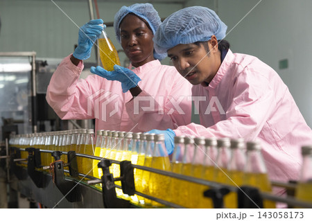 Asian male and black woman factory workers monitoring cold drink bottles on production line at drinks production plant. 143058173